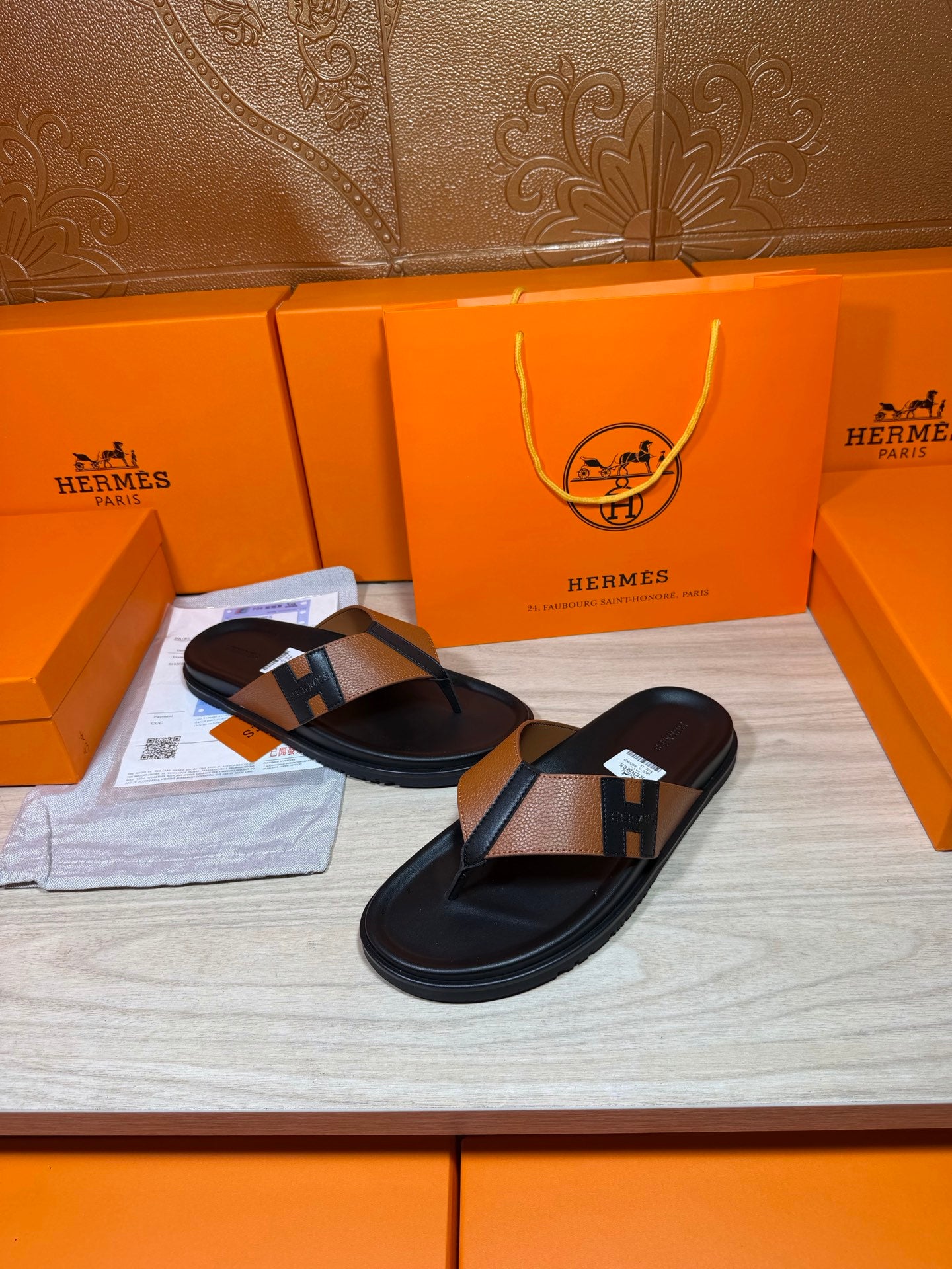 Black thong sandals with tan strap and H buckle detail, open-toe view
