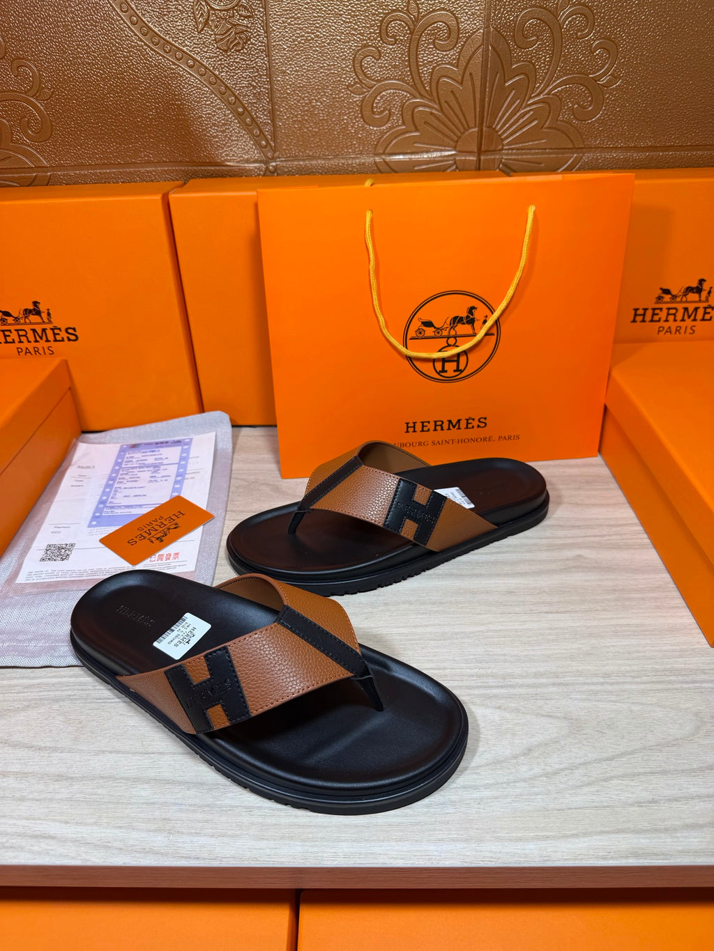 Black thong sandals with tan strap and H buckle detail, front angle