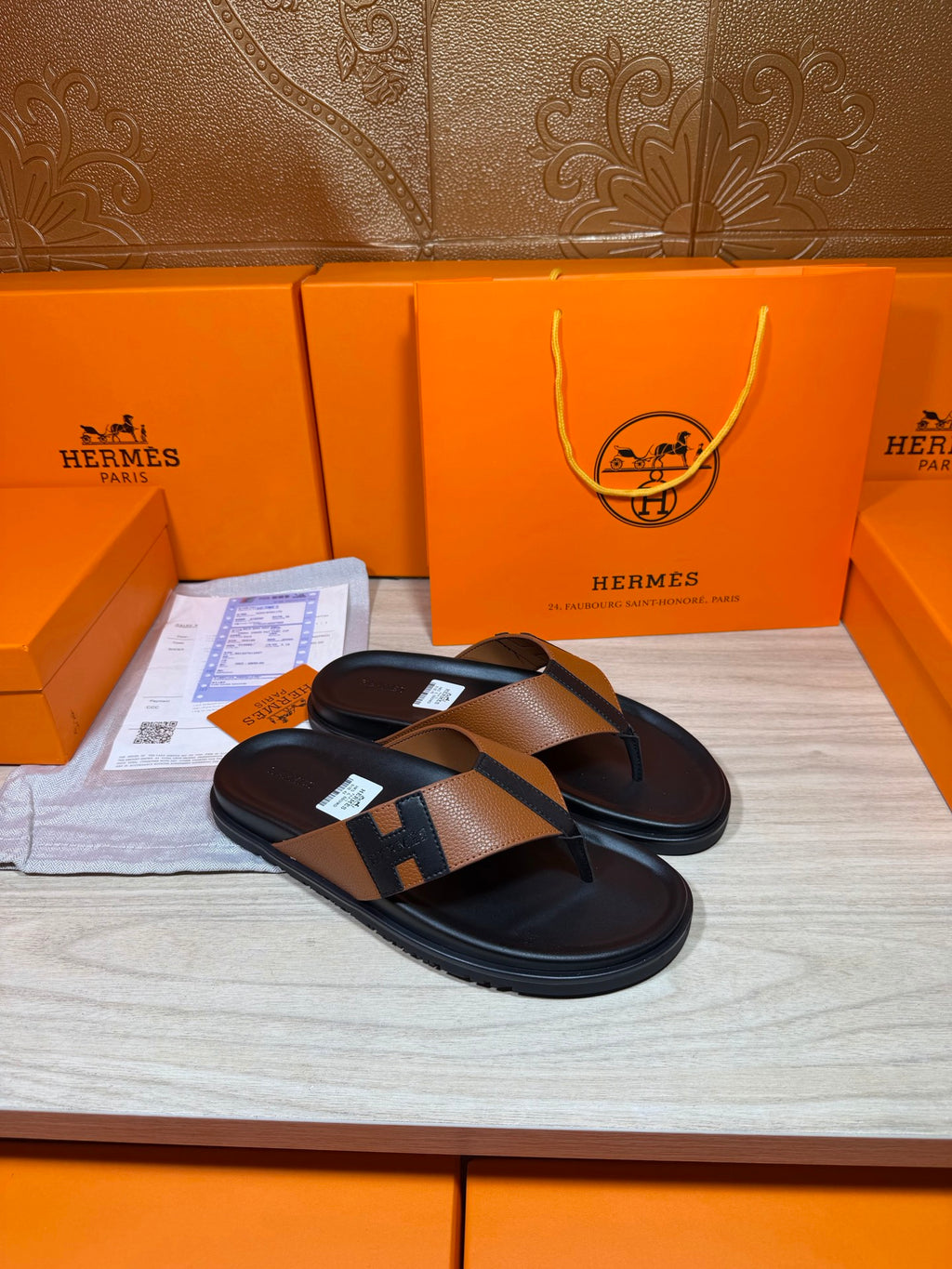 Black thong sandals with tan strap and H buckle detail, angled view