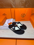 Black thong sandals with white strap panels and square logo buckle detail, laid flat