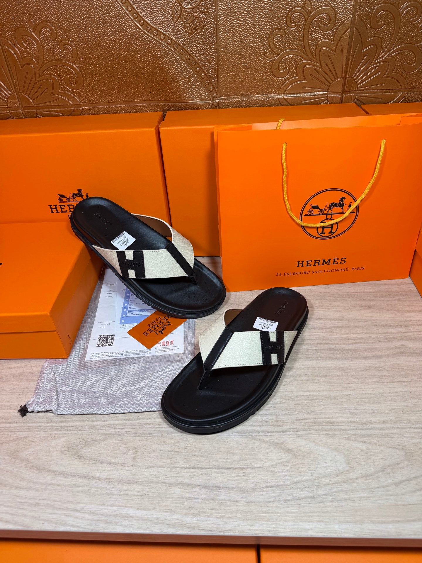Black thong sandals with white strap panels and square logo buckle, shoes side by side
