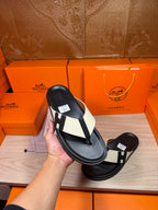 Hand holding a black thong sandal with white strap panels and square logo buckle