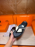 Close view of black thong sandal with white strap panels and square logo buckle in hand