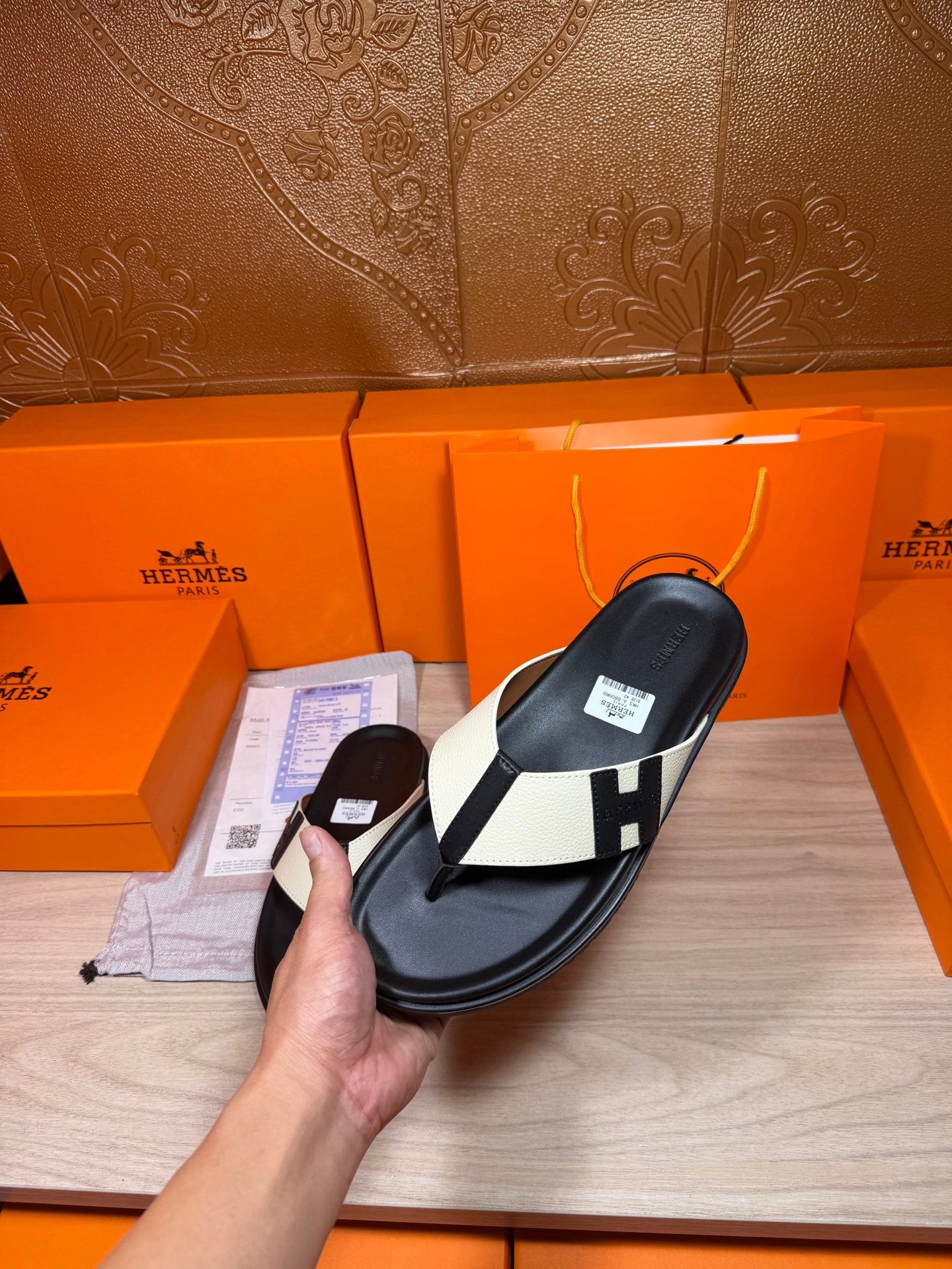 Close view of black thong sandal with white strap panels and square logo buckle in hand