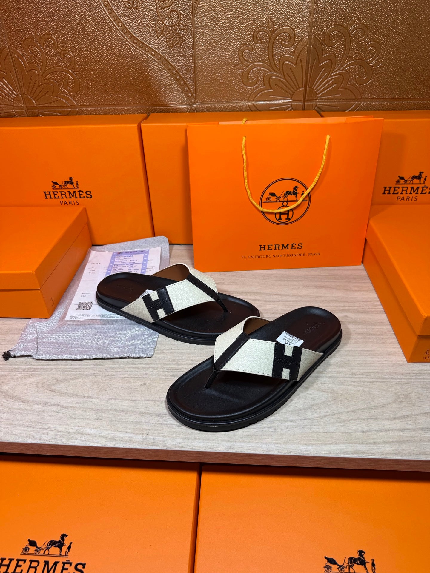 Black thong sandals with white strap panels and square logo buckle, one pair angled