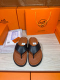 Black leather thong sandals with brown rubber sole, shown paired on display tray