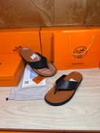 Black leather thong sandals with brown sole, shown with one shoe angled on display