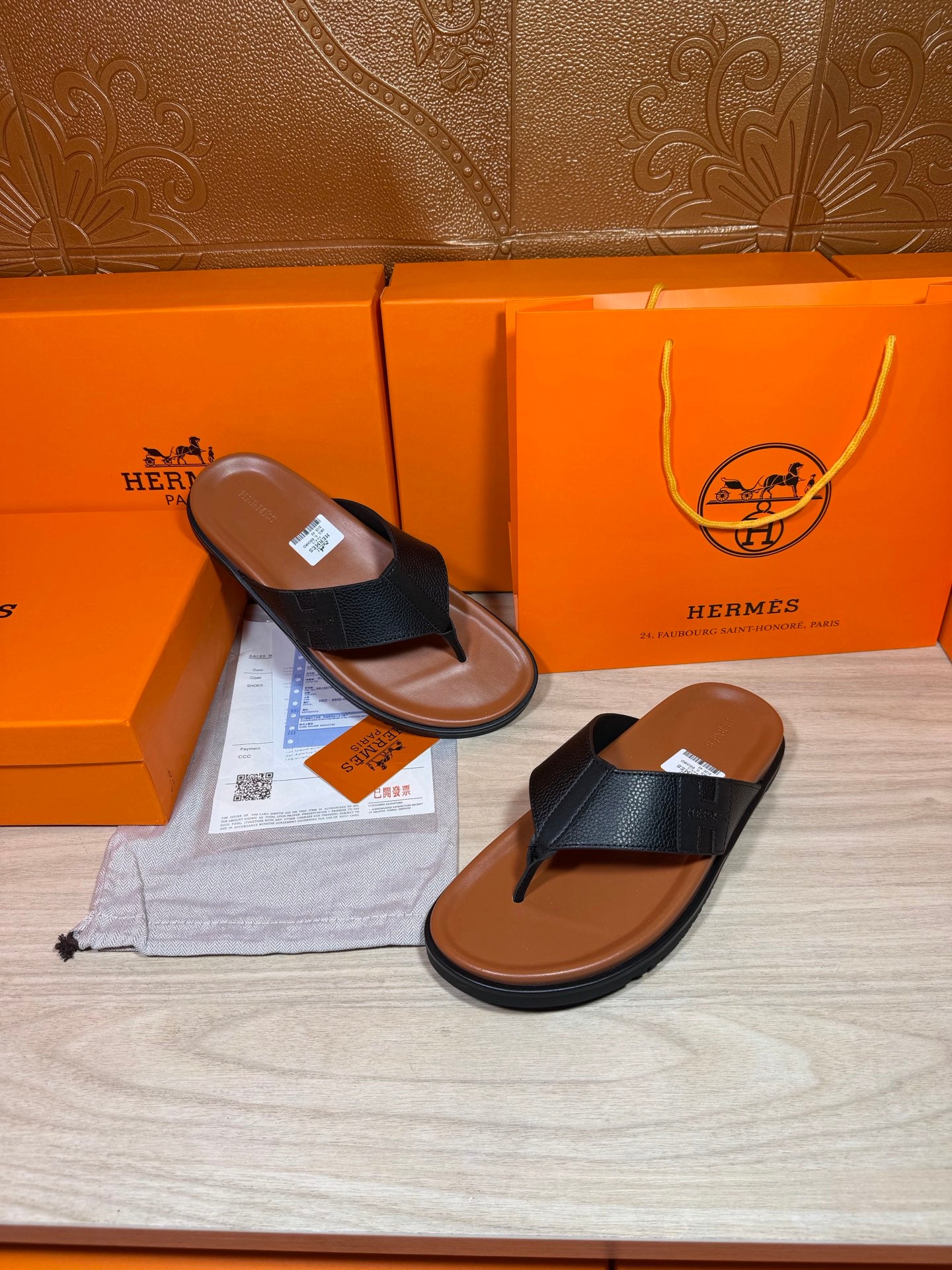 Black leather thong sandals with brown sole, shown with one shoe angled on display