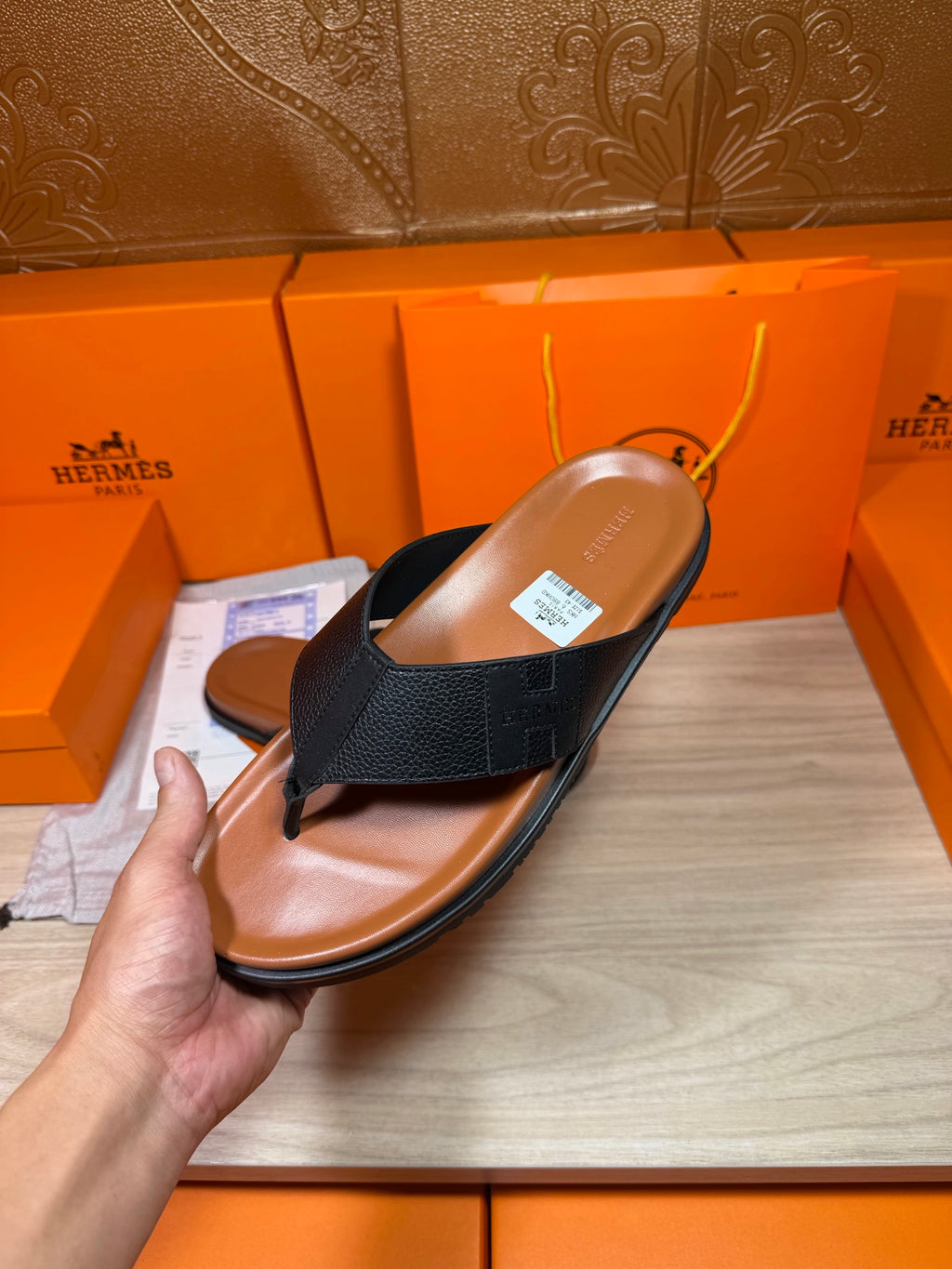 Black leather thong sandal held up, brown sole and insole visible with label