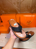Black leather flip-flop sandal held in hand, brown sole and toe post visible
