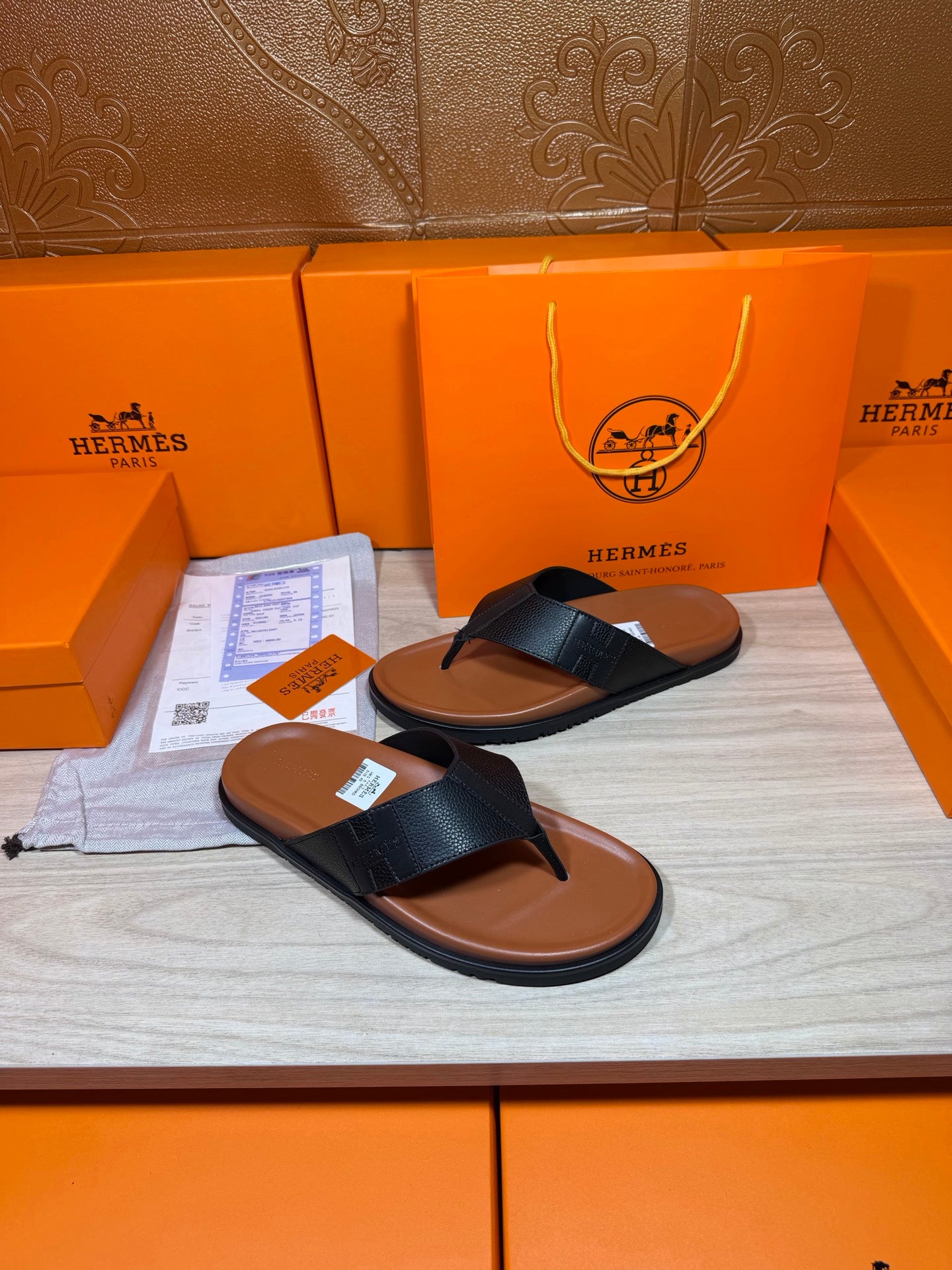 Black leather thong sandals with brown rubber sole, side-by-side on display surface