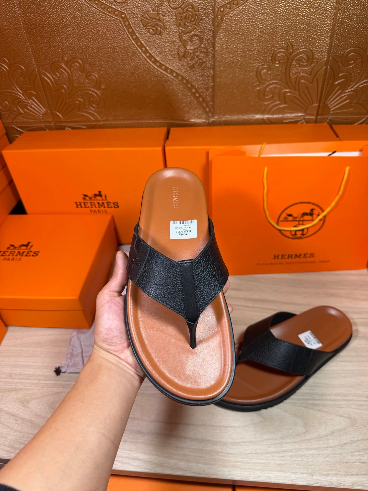 Black leather thong sandal held up front view, brown sole and footbed label visible