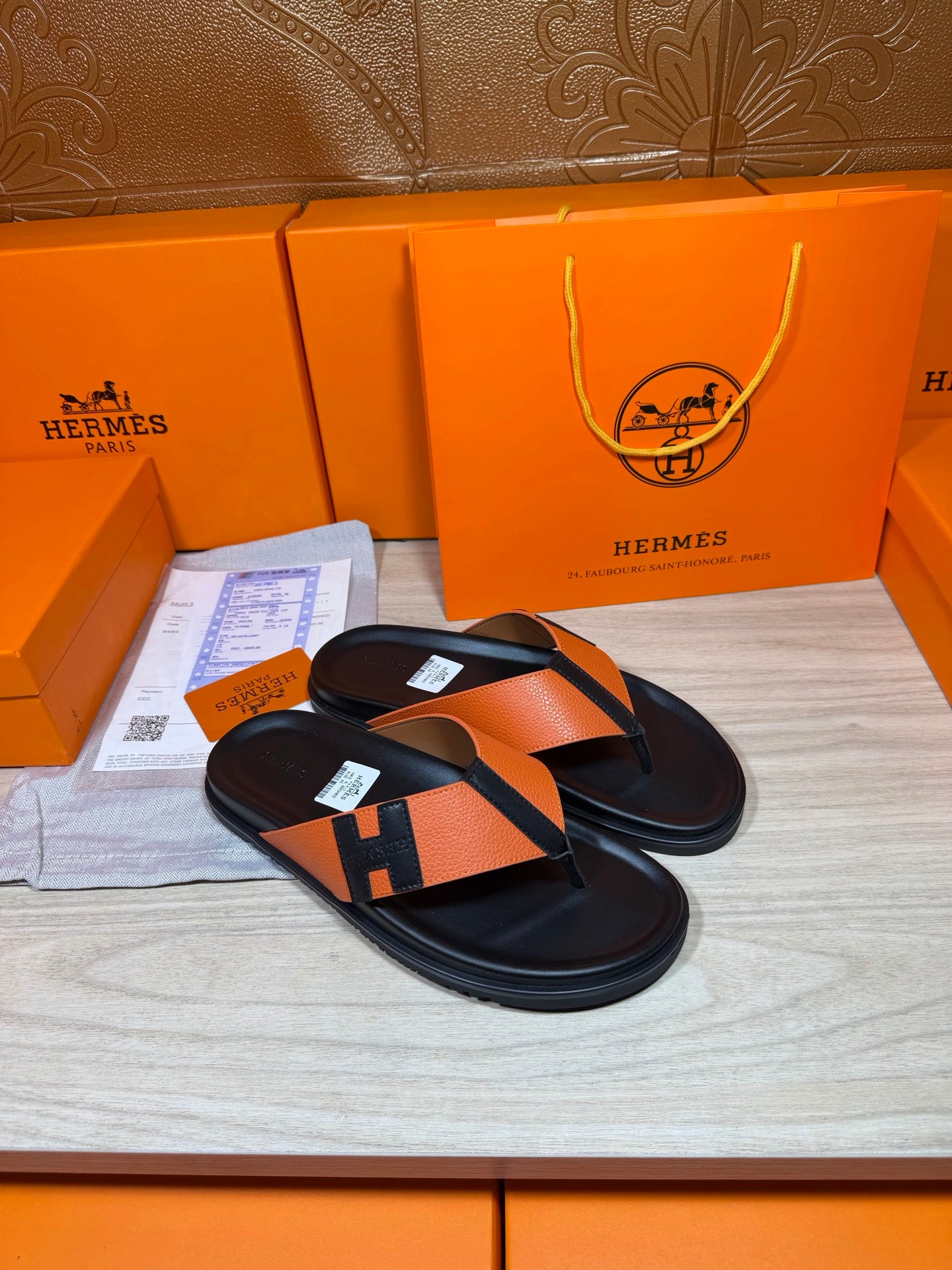H-logo orange strap sandals with black footbed and thong, flat slip-on.