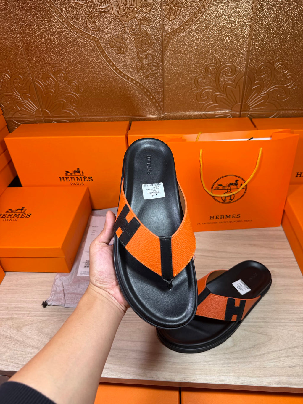 Black sandal with orange H strap and thong, leather footbed, flat sole.