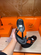 Black sandal with orange H strap and thong, leather footbed, flat sole.