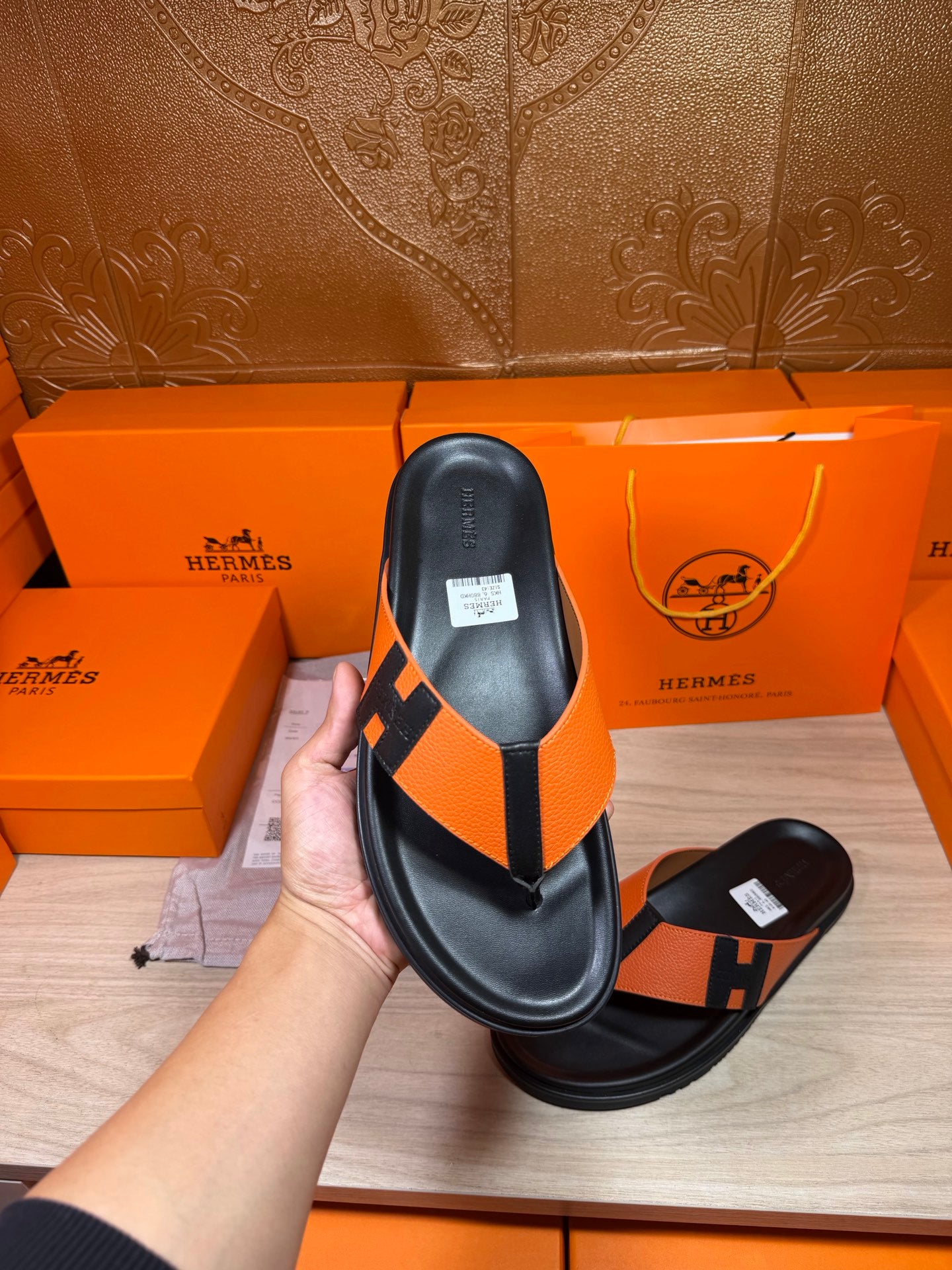 Black sandal with orange H strap and thong, leather footbed, flat sole.