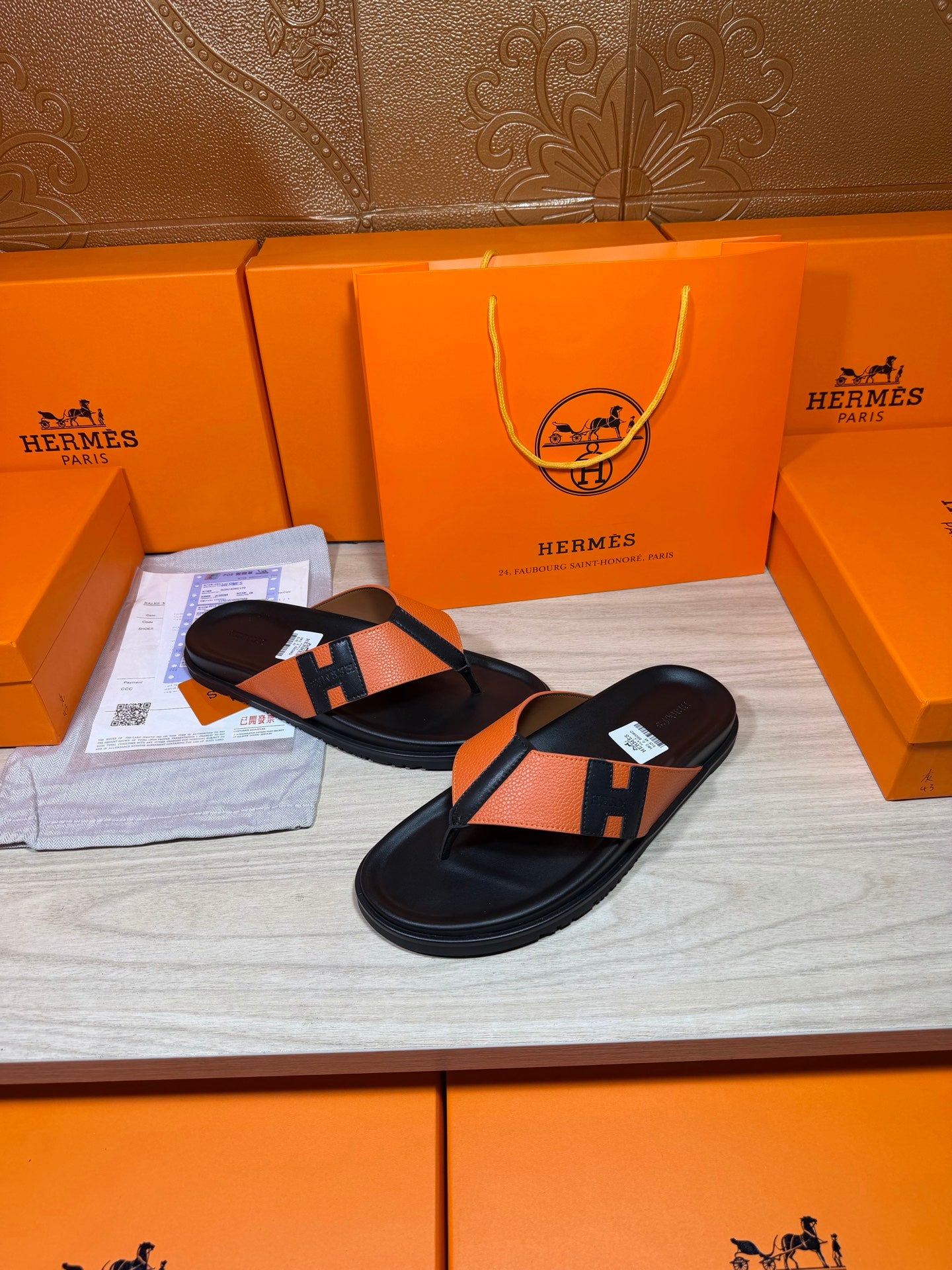 Pair of orange-and-black H sandals with black footbed and wide strap.