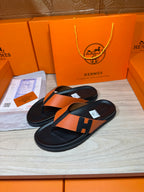 Orange-and-black H logo sandals with black thong straps, flat slide design.