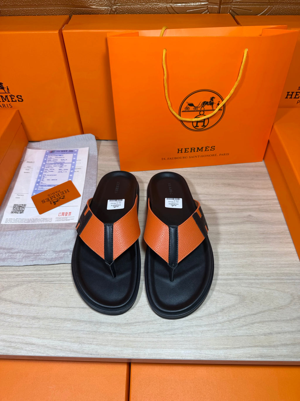 Black leather sandals with orange strap and H buckle, flat flip-flop style.
