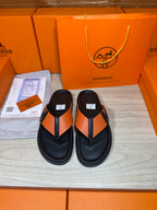 Black leather sandals with orange strap and H buckle, flat flip-flop style.