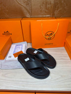 Hermes black leather slide sandals featuring a V-cross strap and cushioned sole.