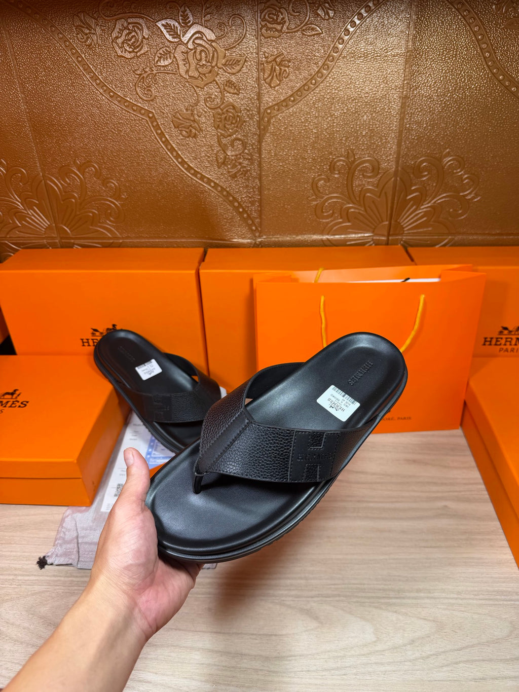 Hermes black leather slide sandals held in hand, with cross strap and flat sole.