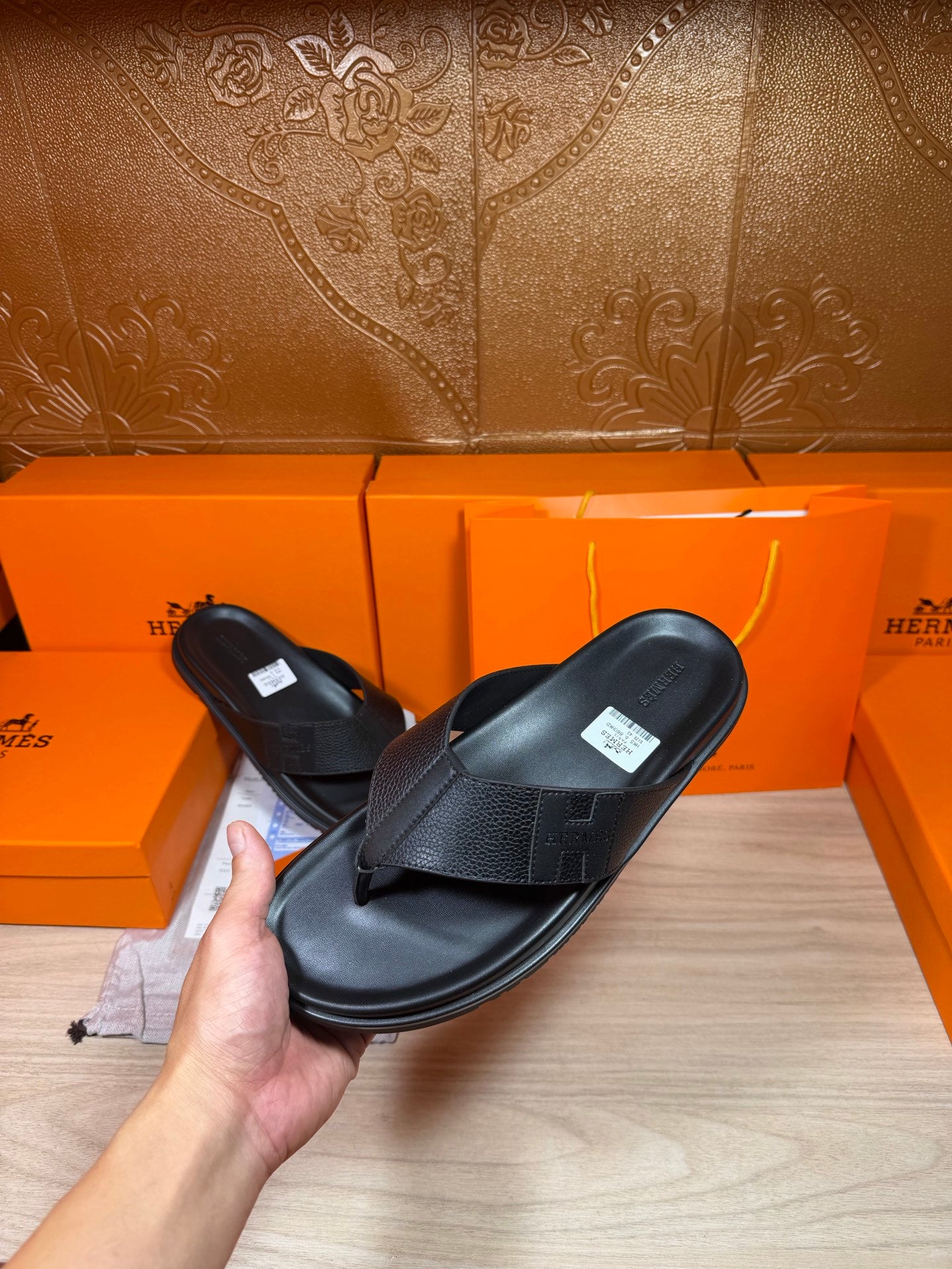 Hermes black leather slide sandals held in hand, with cross strap and flat sole.