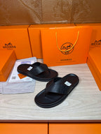 Hermes black leather thong slide sandals with textured strap and flat sole.