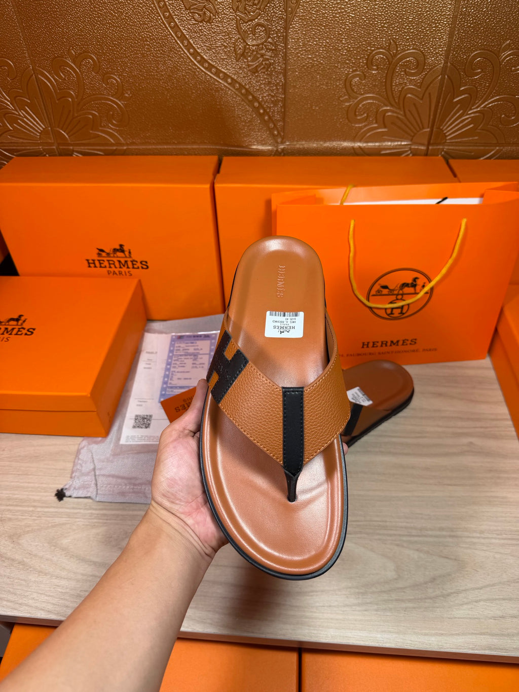 Brown leather thong sandal held in hand with dark H strap and flat sole