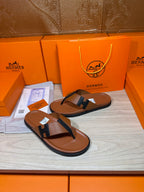 Brown leather thong sandals with dark H strap, shown on a wooden display surface