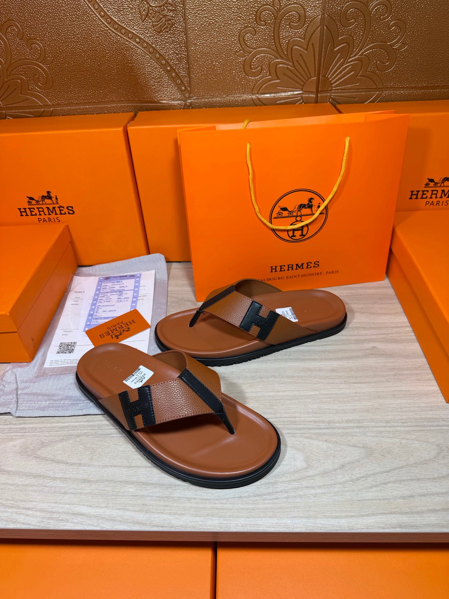 Brown leather thong sandals with dark H strap, shown on a wooden display surface