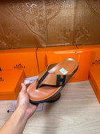 Brown leather thong sandal held in hand, dark H strap and flat sole