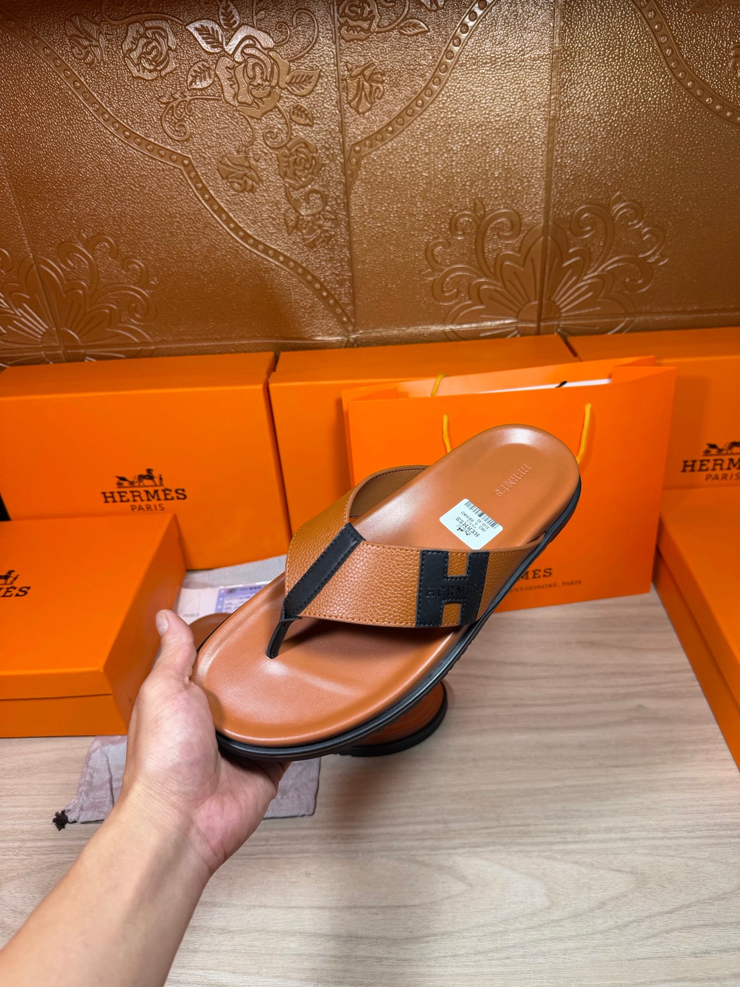 Brown leather thong sandal held in hand, dark H strap and flat sole