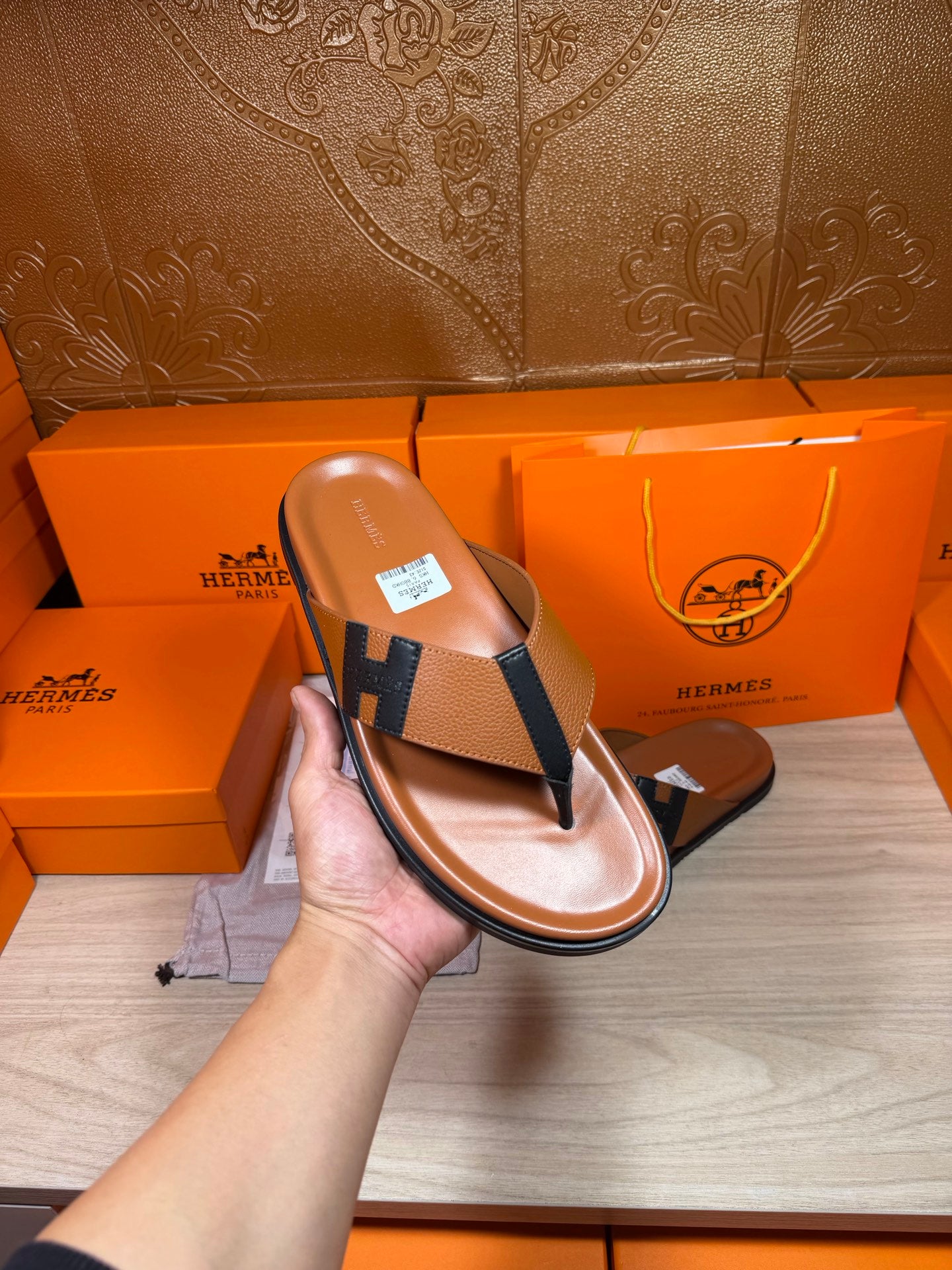Brown leather flip-flop sandal held up, dark H strap on a textured footbed