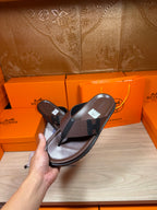 Dark leather thong sandal in hand with textured top strap and flat sole