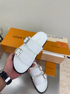 White Louis Vuitton buckle sandals held in hand, embossed strap detail and silver tabs