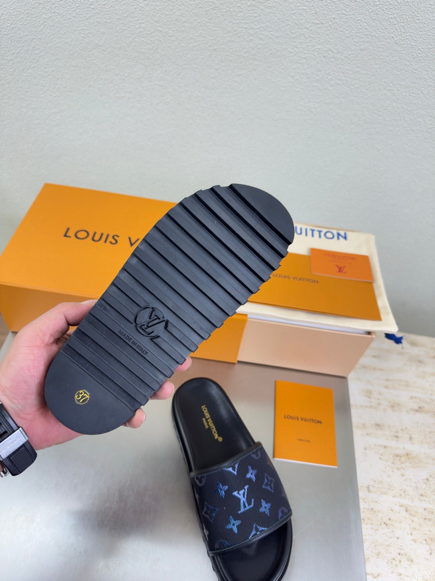 Louis Vuitton sandals shown from sole, dark rubber tread with embossed logo