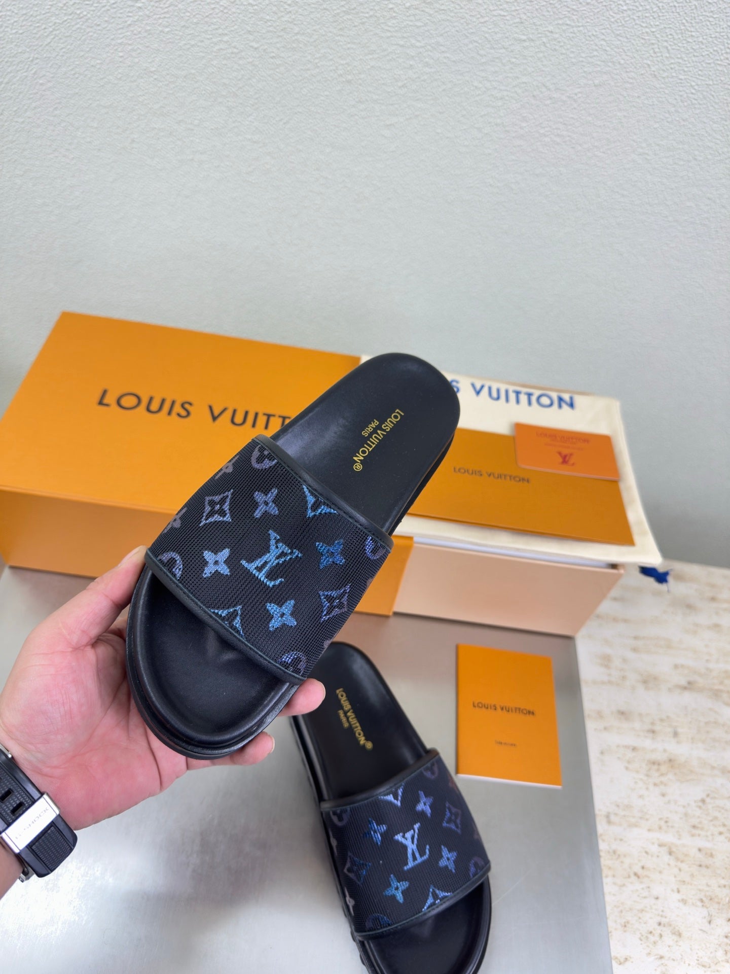 Louis Vuitton slide sandals held in hand, dark navy with blue monogram print