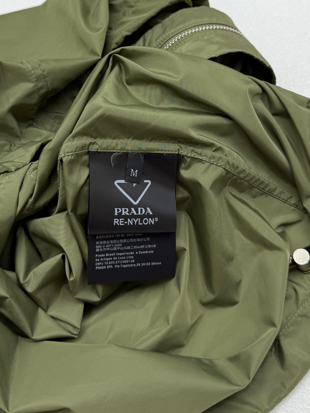 Olive green short-sleeve zip jacket interior with PRADA RE-NYLON care label.