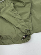 Olive green short-sleeve zip jacket front corner with metal ring pull and stitching.