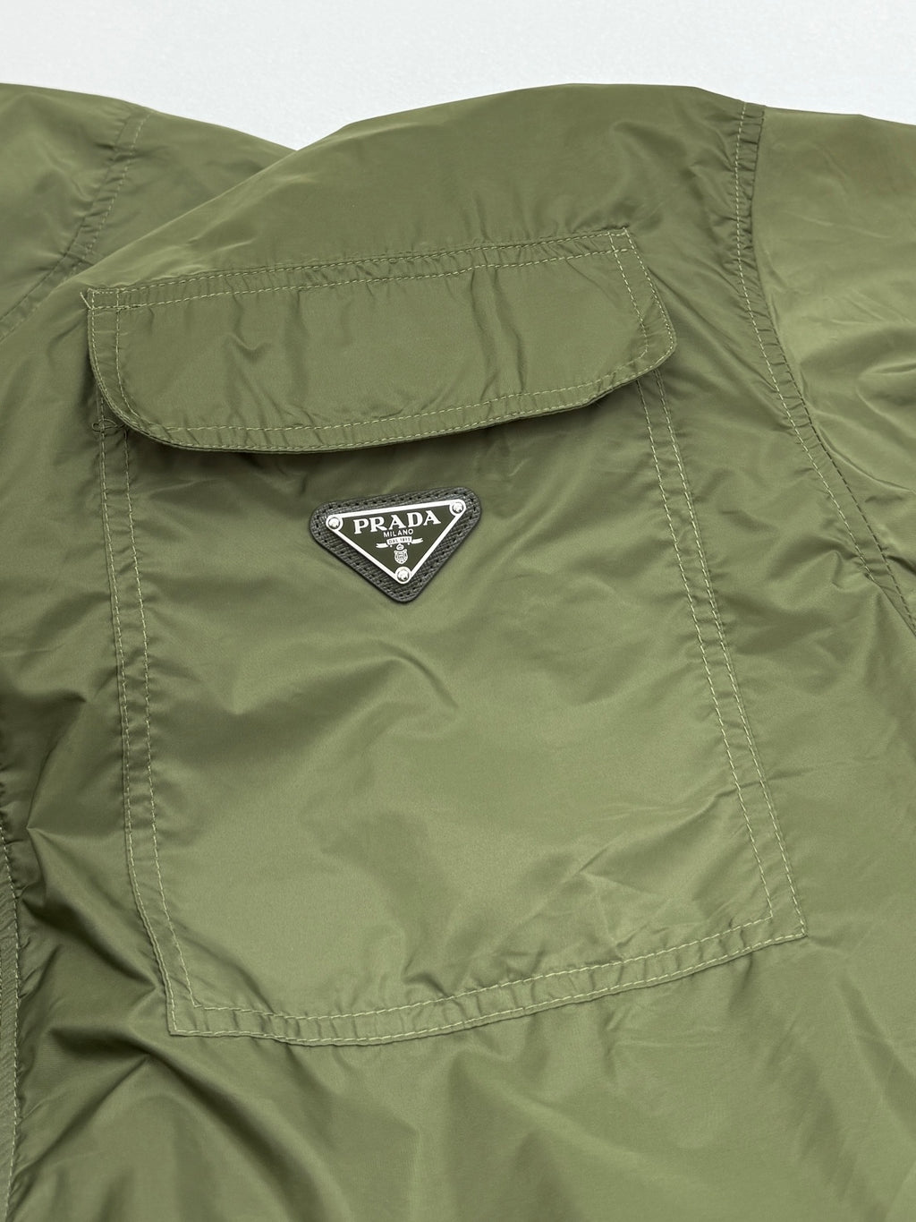 Olive green short-sleeve zip jacket with Prada triangle logo on a chest flap pocket.