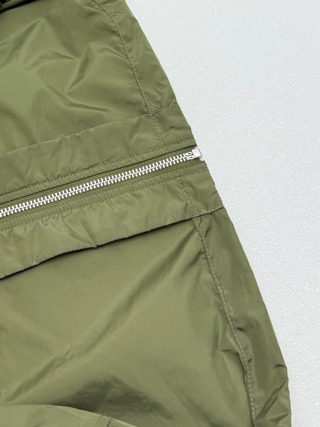Olive green short-sleeve zip jacket side panel with metal zipper and seam stitching.