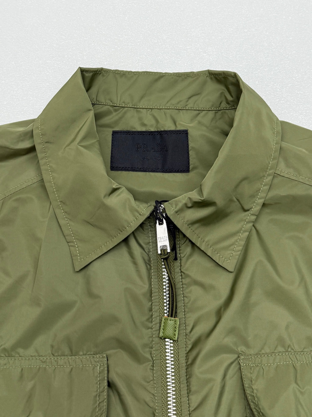 Olive green short-sleeve zip jacket with structured collar and silver zipper pull.