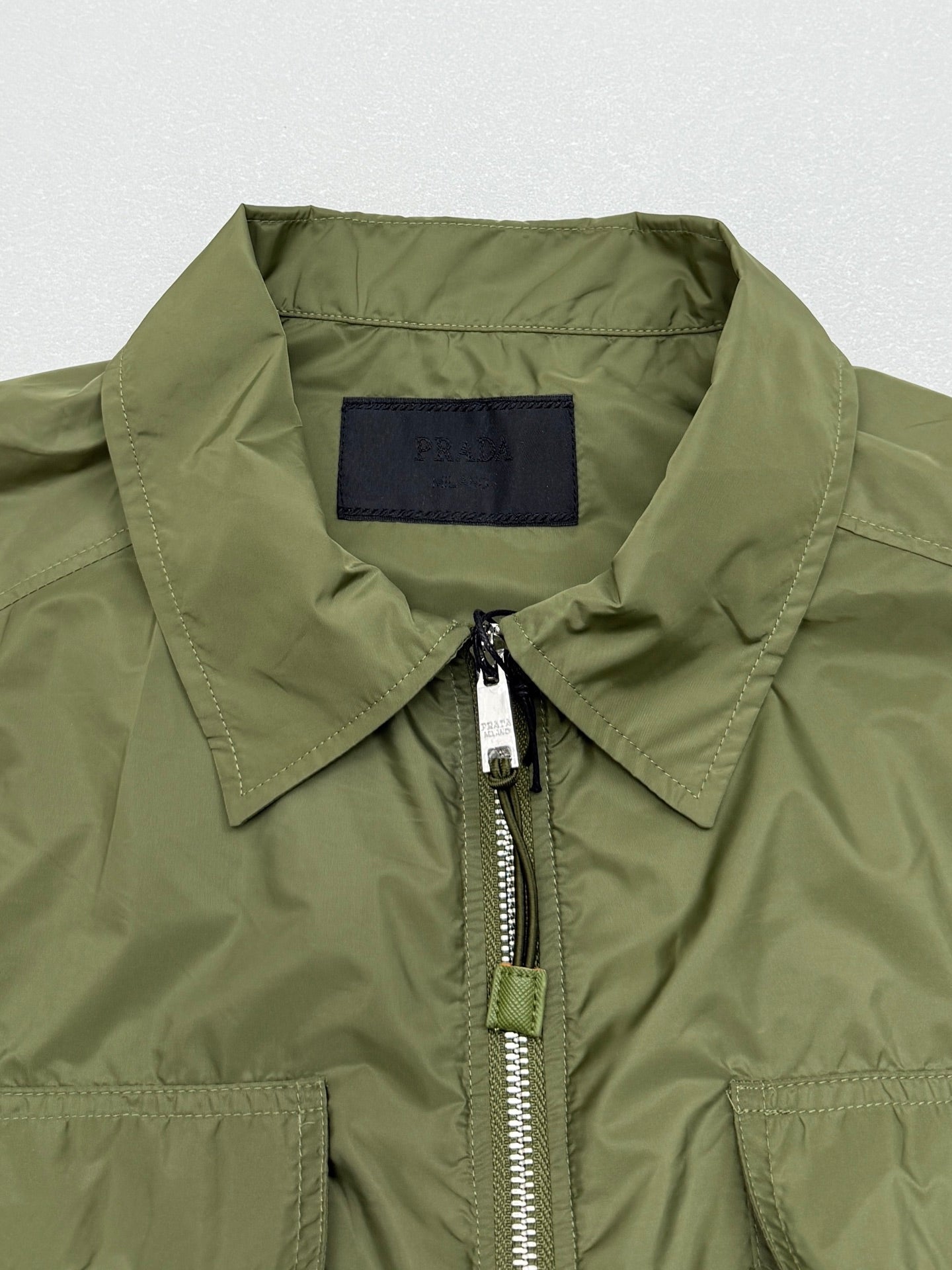 Olive green short-sleeve zip jacket with structured collar and silver zipper pull.
