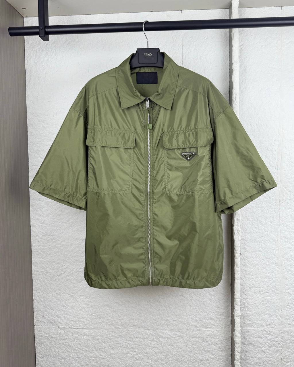Olive green short-sleeve zip jacket with two chest pockets and Prada triangle logo.