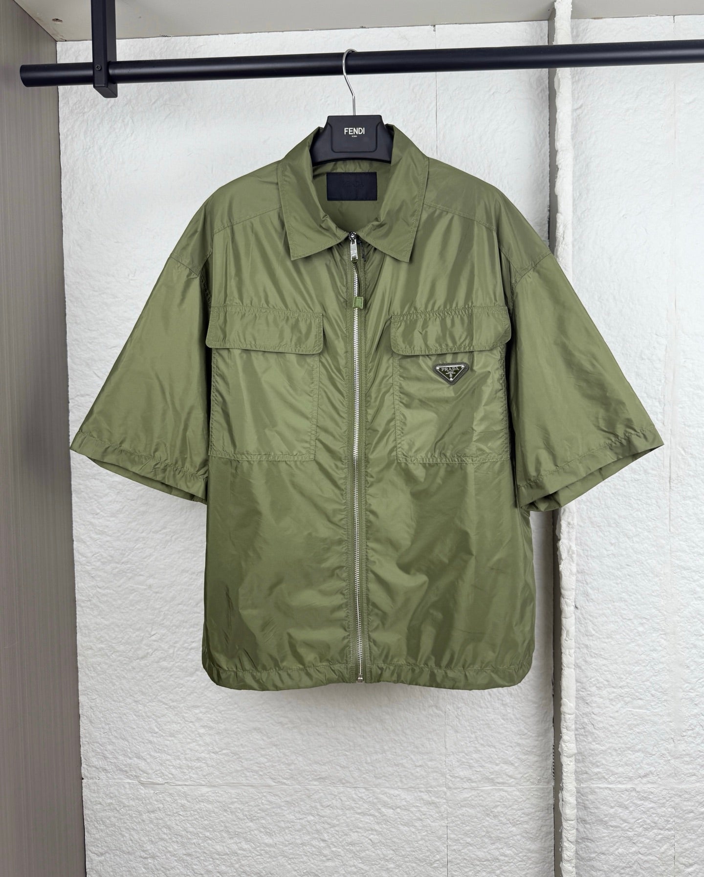 Olive green short-sleeve zip jacket with two chest pockets and Prada triangle logo.