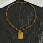Gold-tone charm pendant necklace with circular linked chain and tag charm.