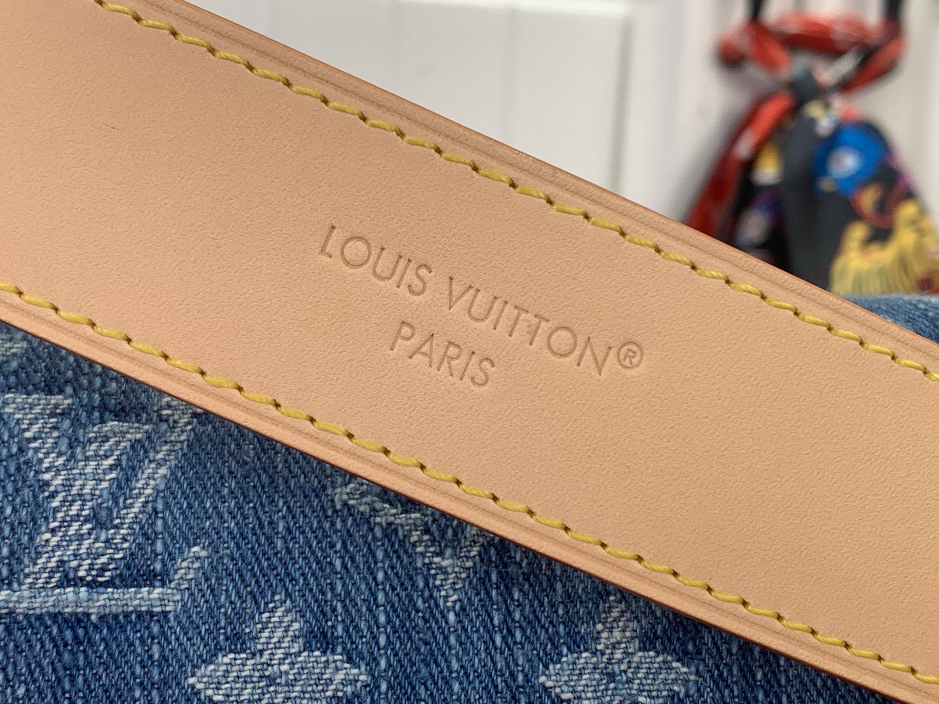 Tan leather trim with embossed text and yellow stitching on blue monogram denim