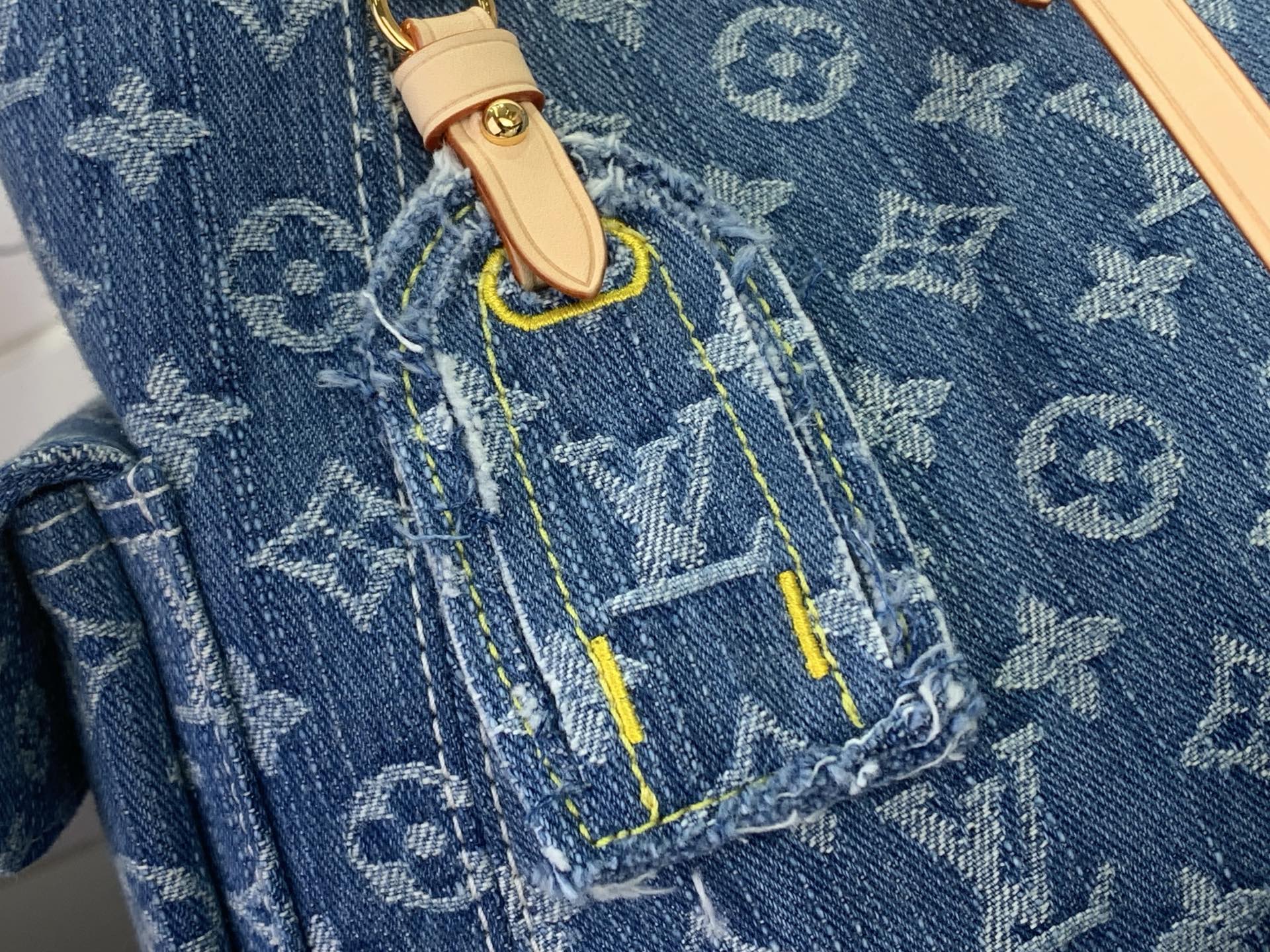Blue monogram denim panel with tan tab, topstitching, and small gold snap