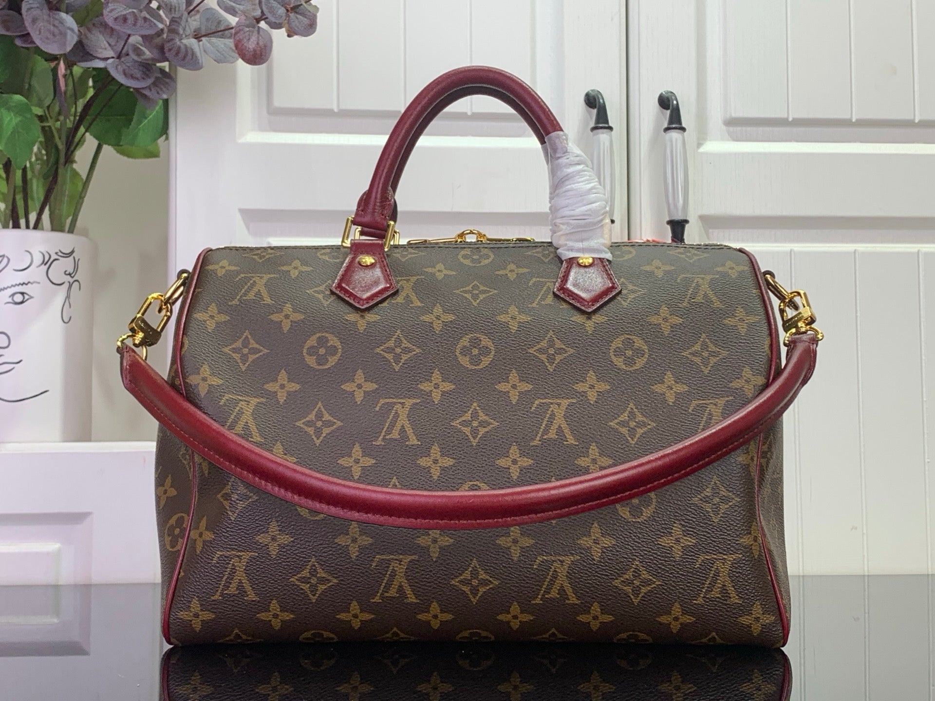 Monogram top-handle bag with burgundy handles and gold side hardware